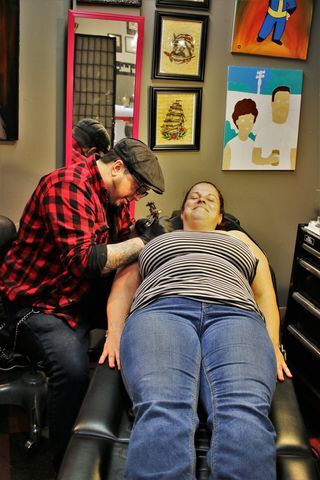 <em>Tattoo artist, Jason, working on a tattoo for Jamie.</em>
<strong>Photo by <a href=