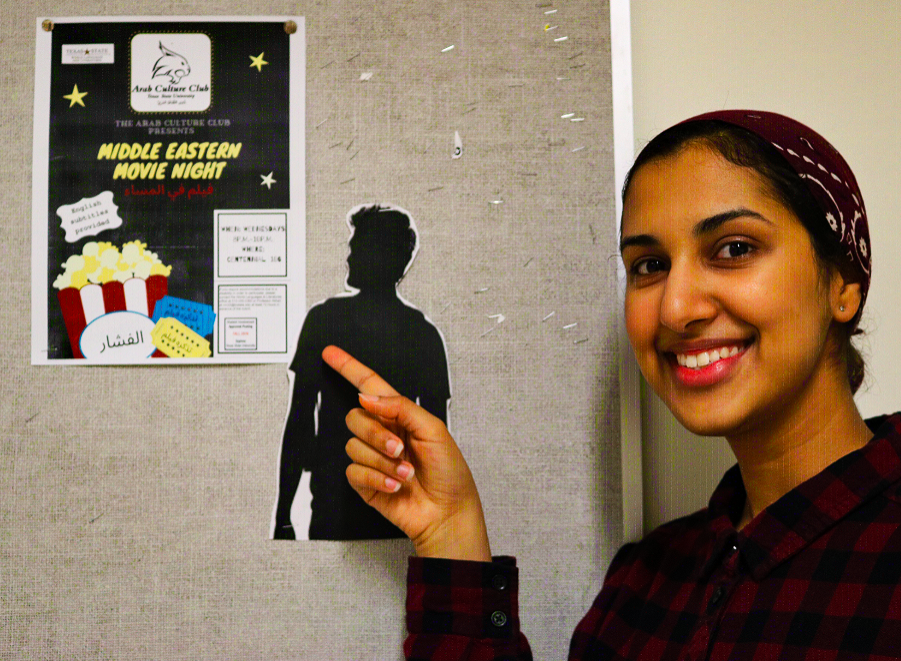 President of ACC and communication studies senior Dania Sherian pointing to one of the club’s Middle Eastern Movie Night flyers. Photo credit: Abby Gutierrez