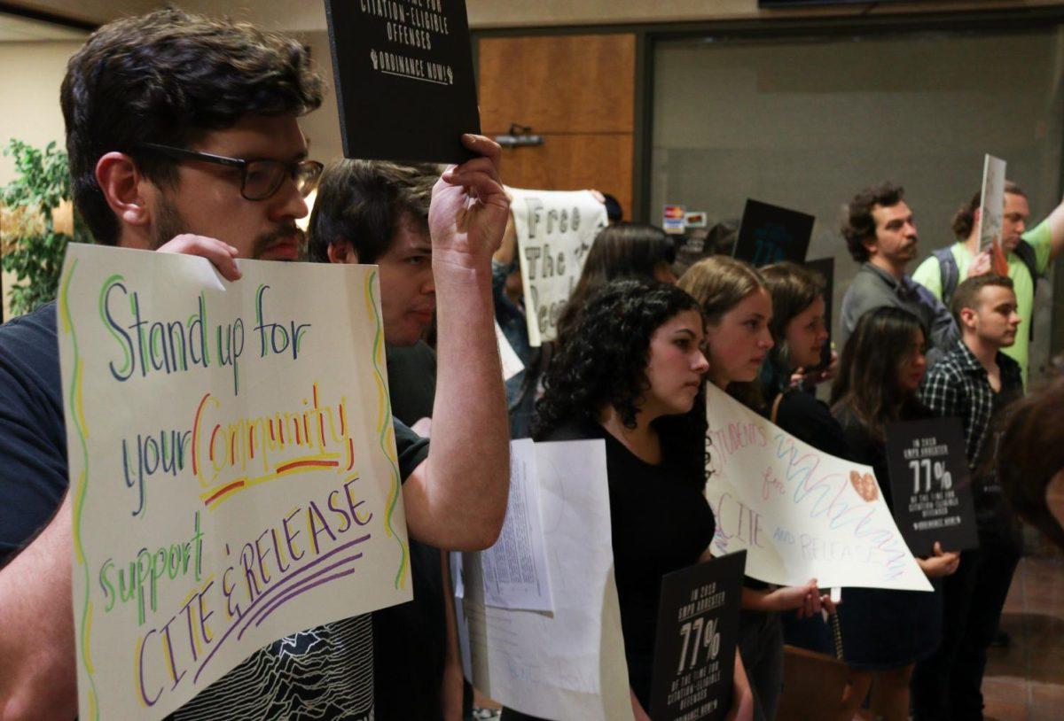Texas State applied sociology senior August Kutac (left) holds a sign advocating for a new cite and release ordinance Tuesday, March 3, 2020, and the City Council meeting at City Hall.