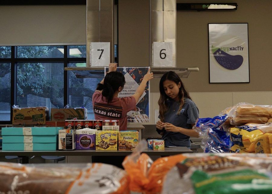 Texas State pre-nursing sophomores Andrea Poblete (left) and Sofia Yanez hang an informational poster about an upcoming event at the Bobcat Bounty food pantry Oct. 24, 2019, in the Family and Consumer Sciences building. Included among student workers are Bobcat Bounty workers, Alkek library workers, ITAC assistants and more.