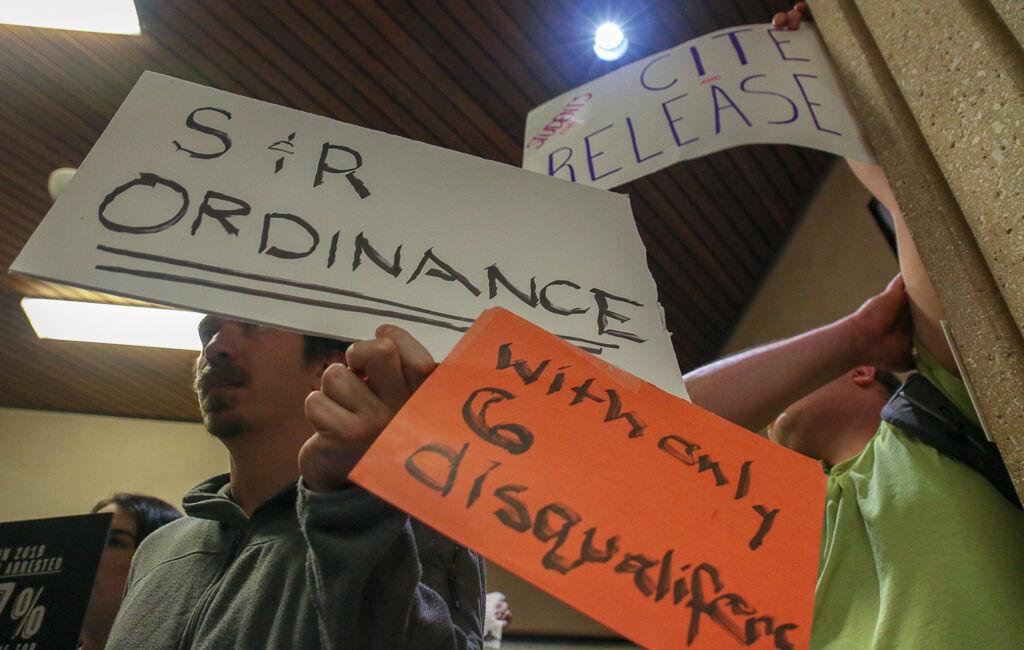 (Left to right) Austin Adams and John Matthew Redding hold up signs advocating for the implementation of a cite-and-release ordinance in San Marcos, Tuesday, March 3, 2020, outside of a city council meeting at City Hall.