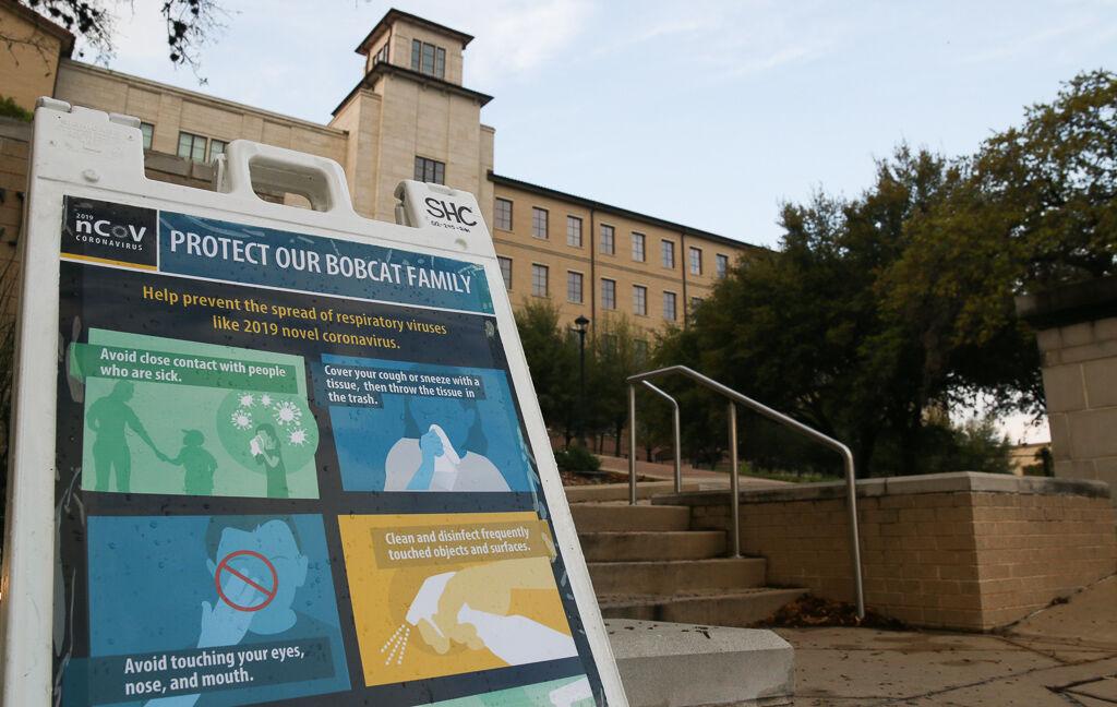 A file photo of a sign with instructions for helping reduce the spread of COVID-19, sitting near the Undergraduate Academic Center building at Texas State.