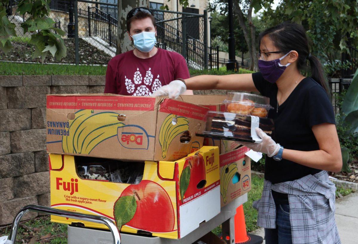 Archeology graduate student Kaylee Gaumnitz (right) reaches for food to provide for those attending a Bobcat Bounty distribution, Thursday, Sept. 10, 2020, outside of the Family and Consumer Sciences building. Human nutrition graduate student Travis Luzania (left) worked beforehand, wheeling carts of food out to the parking lot.