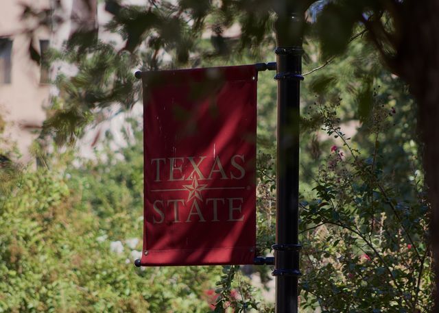 A small, red banner with the words “Texas State” hangs from a light post.