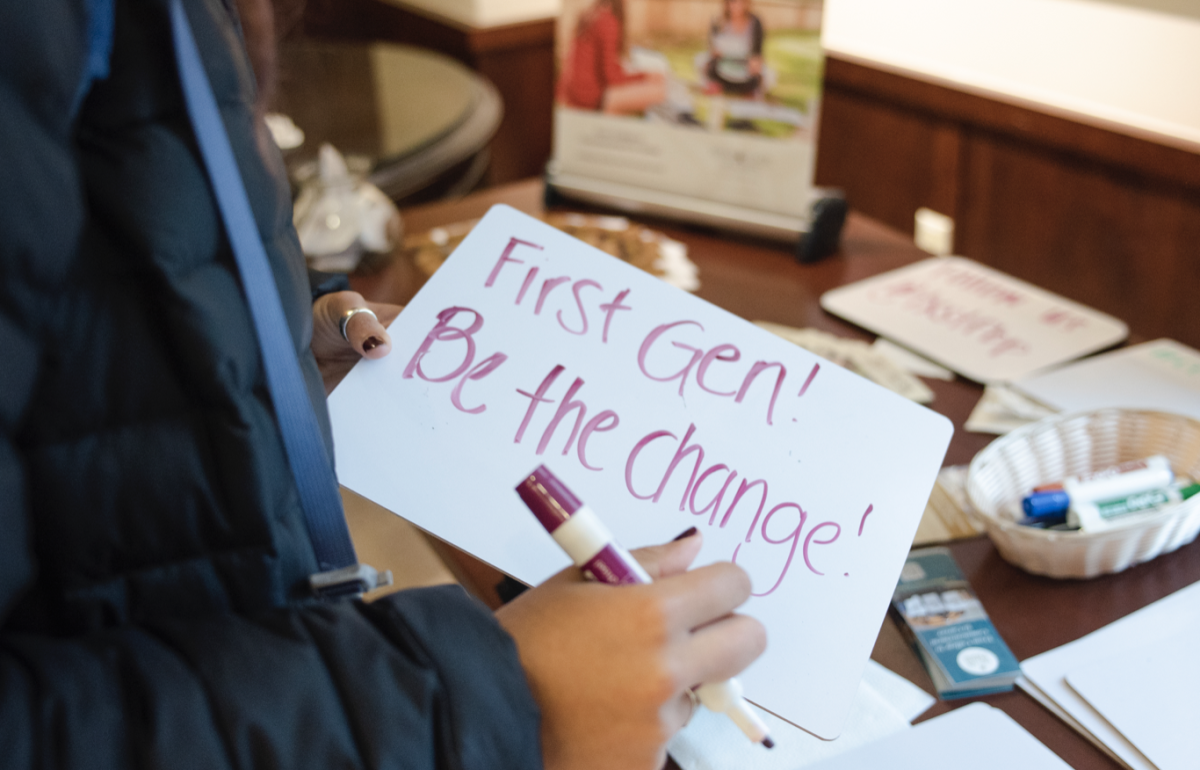 A student writes First Gen! Be the Change! on a small white board during a previous First-Gen Week event.