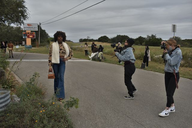 FMA model Brittyne LaMothe walks down the street as videographer Melina Madrigal (left) and photographer Hanna Hurd (right) film and photograph her outfit while stylists observe behind the camera in Wimberly, Texas.