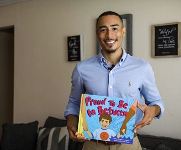 Alumnus and author Marcus Peoples holds a copy of his new childrens book, Proud to be in Between, which tells the story of a child born to interracial parents