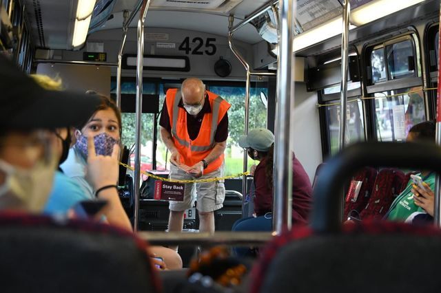 Students and a driver socialize on board a shuttle while it is stopped, Tuesday, Aug. 25, 2020, at the University Tower bus stop. In accordance with COVID-19 policy, passengers are wearing masks and social distancing.