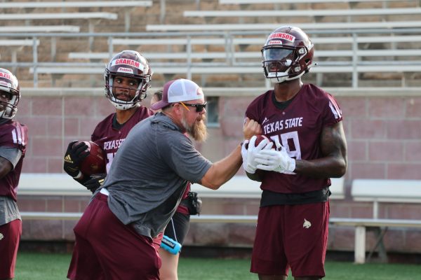 Tight end coach Brain Hamilton attempts to hit the football out of junior wide receiver Dennis Robinson's (19) hands during a drill, Friday, Aug. 6, 2021, at Bobcat Stadium.