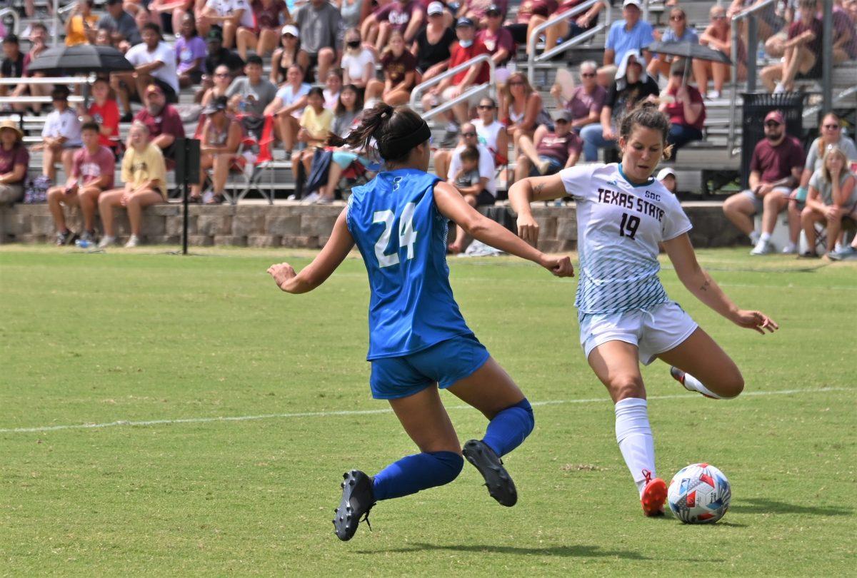 Texas State sophomore midfielder Haley Shaw (19) prepares to kick the ball while Texas A&M-Corpus Christi junior defender Maddie Janolo (24) advances, Sunday, Sept. 12, 2021, at Bobcat Soccer Complex. The Bobcats won 4-0.