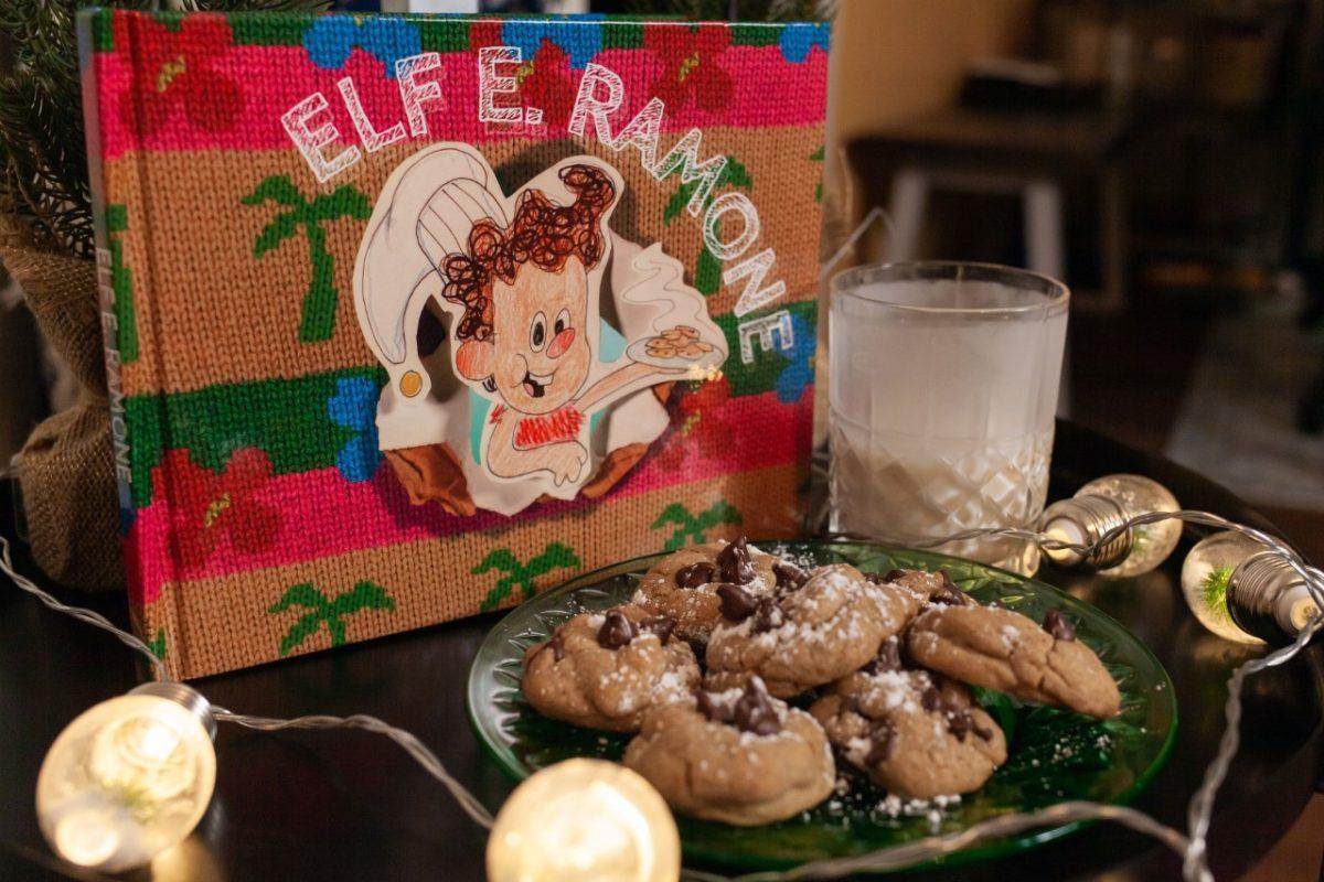Elf E. Ramone stands behind a plate of cookies and a glass of milk. The childrens book tells the story of the elf who started the Christmas Eve tradition of leaving cookies and milk for Santa.