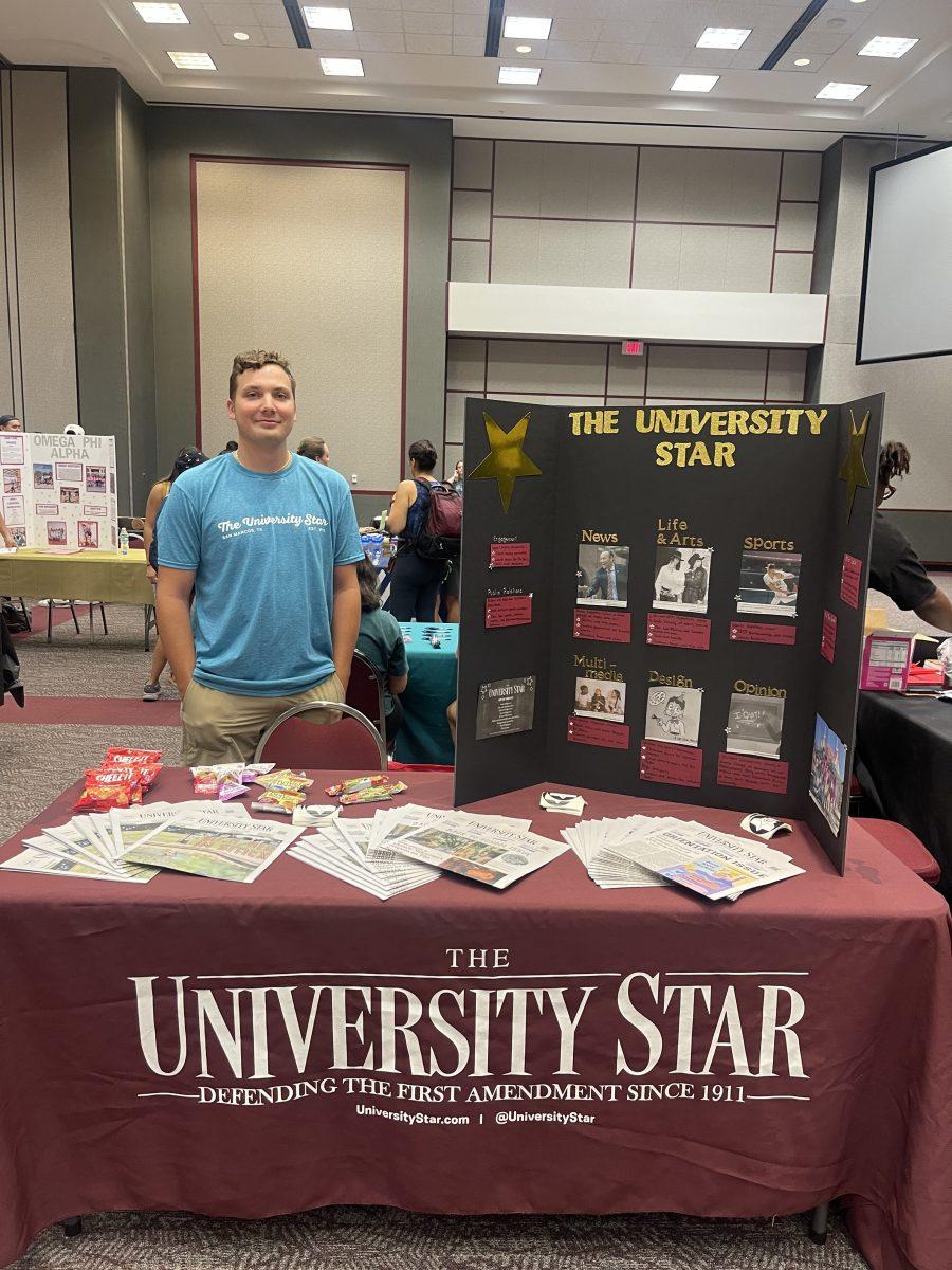 Texas State journalism senior Dillon Strine poses with The University Star table at a recruiting event, Monday, Aug. 29, 2022, at the LBJ Ballroom.