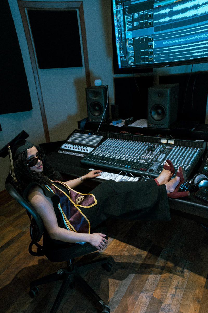 Texas State alumna Jaelen Miah Lopez poses in her cap and gown in a recording studio, April 2023, at Fire Station Studios.