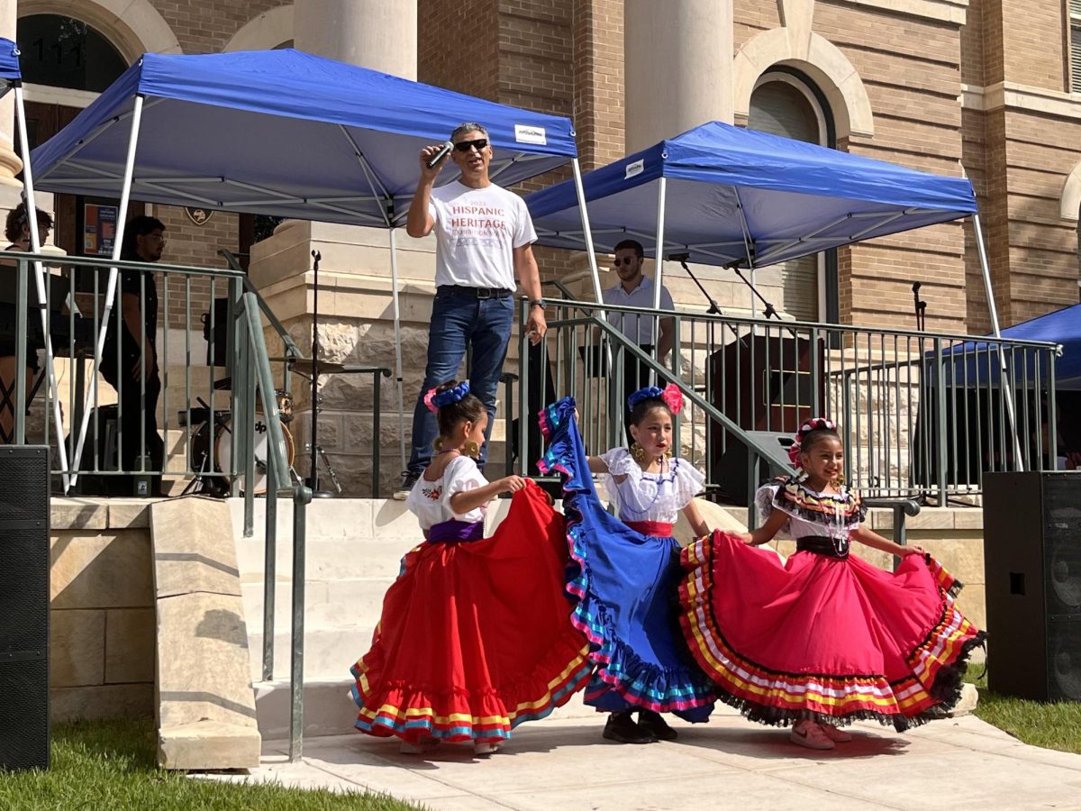 Hays County Judge Ruben Becerra giving a speech with three dancers from Compañia de Danza Folklórica, a dance company in New Braunfels, in front of him, Saturday, Sept. 16, 2023, at the Hispanic Heritage Exhibition Walk, hosted at Hays County Courthouse in San Marcos.