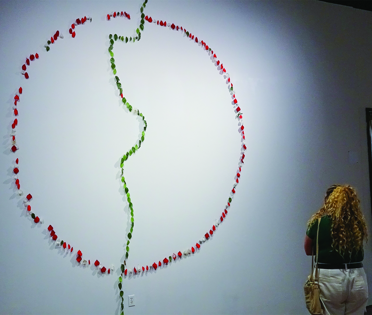Journalism sophomore Breanna Lopez looks at a large-scale installation of plastic cemetery flowers on the wall, Wednesday, Sept. 20, 2023, at the The Unsettlements: Moms exhibition at Texas State Galleries.