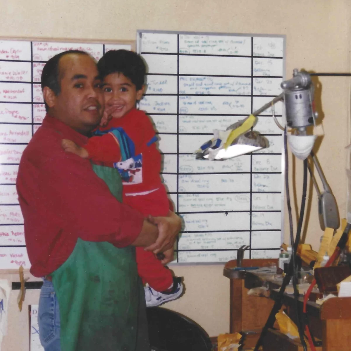 Robert Jimenez (left) carries his son Adam Jimenez (right) while making jewelry at the first shop for San Jose Jewelers, 1995, in Waco, Texas.
