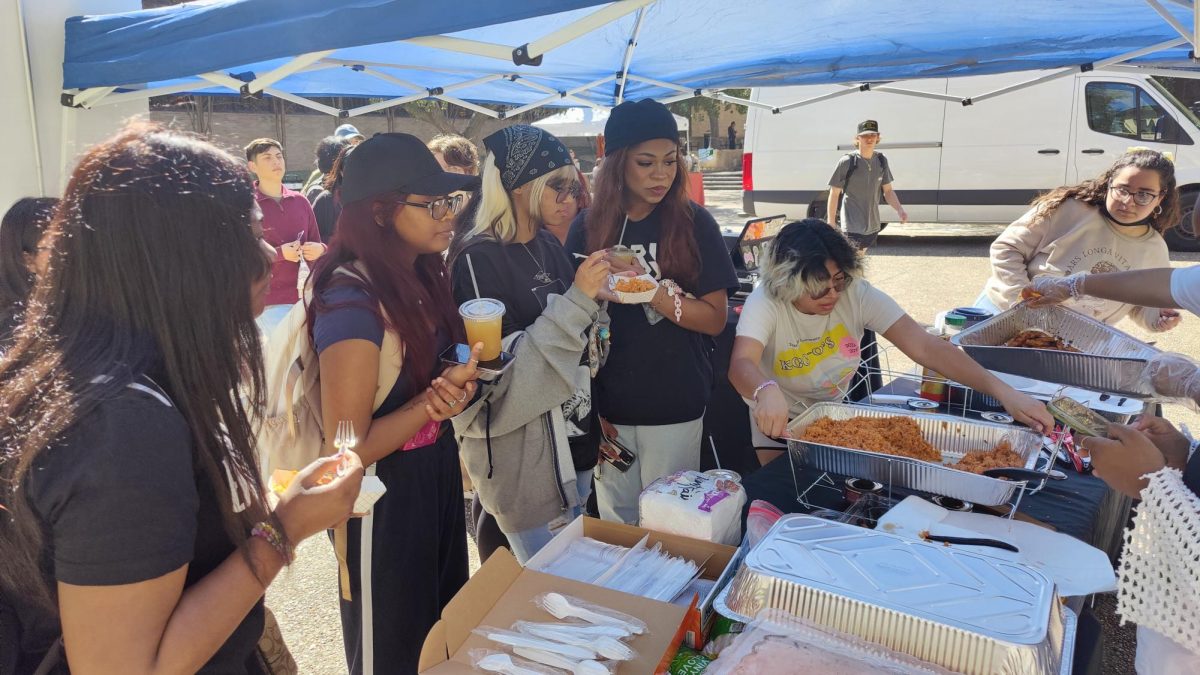 Students eat their food under the Korean Culture Club Marketplace booth, Thursday, Feb. 22, 2024, at The Quad.
