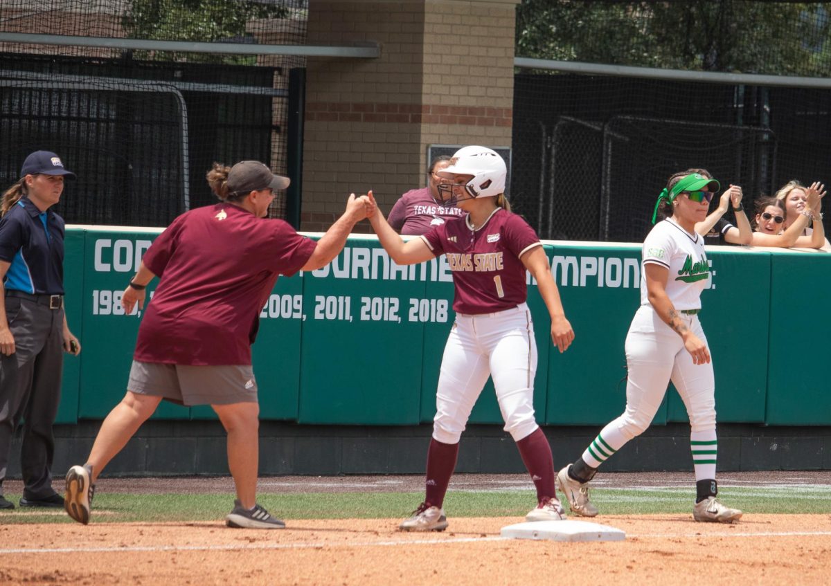 Texas State sophomore designated player Emilee Baker (1) celebrates a third base run with her coach during the game against Marshall, Friday, May 10, 2024, at Bobcat Softball Stadium.