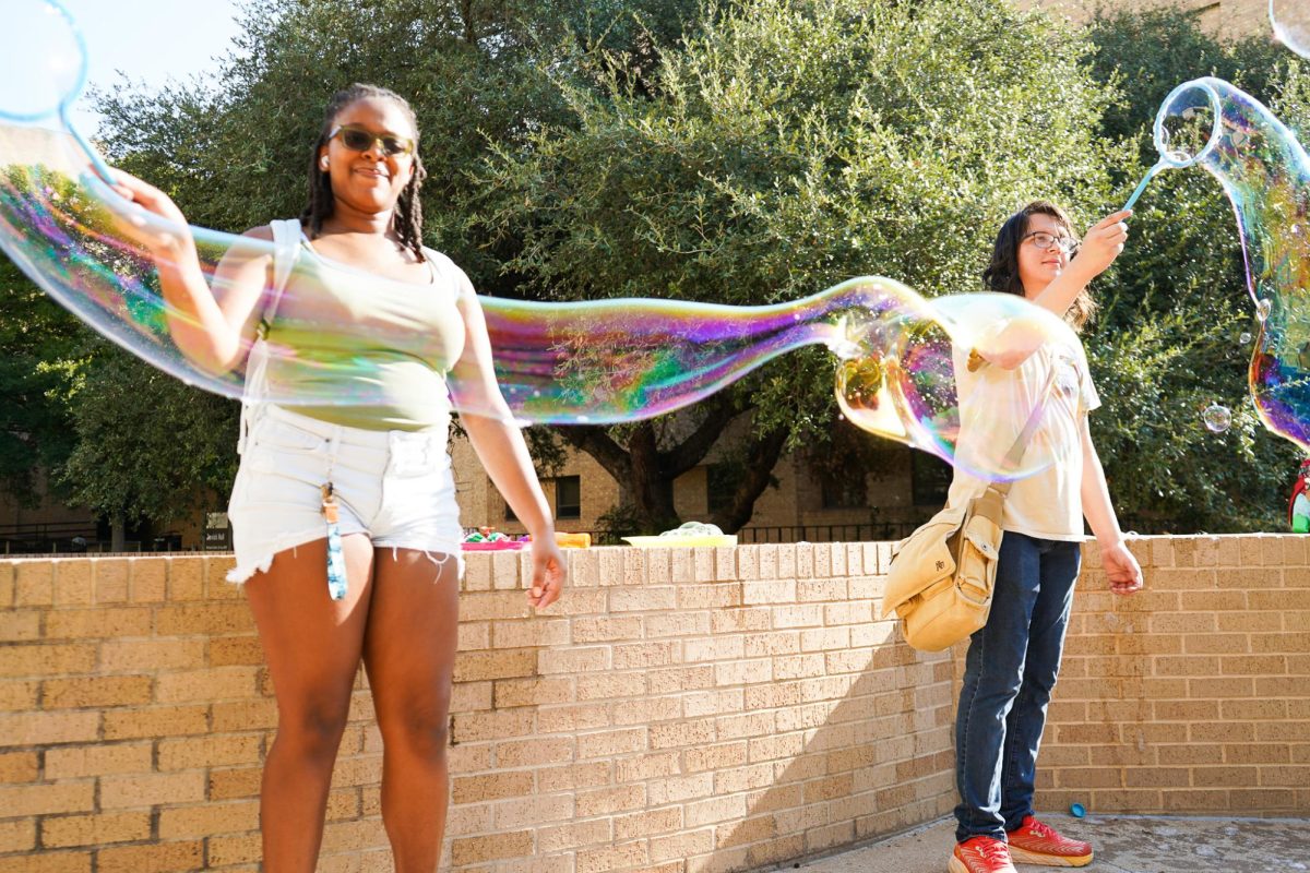 (Left) Biology sophomore Carli Marshall and (right) interior design freshman Aiden Peterson wave bubbles at students walking to their first day of classes, Monday, Aug. 26, 2024, outside Derrick Hall.