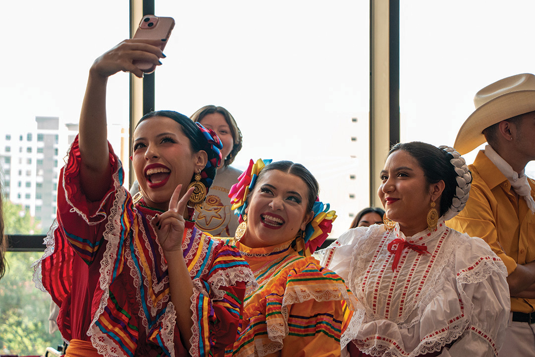 Three members of Grupo Folklorico Ocotochtli wearing vestido de listones (dress of ribons) pose for a selfie before dancing at Viva TXST on Monday, Sept. 16, 2024, at the LBJ Student Center. Established in 1983, Grupo Folklorico Ocotochtli shares the culture of Mexico through dance.