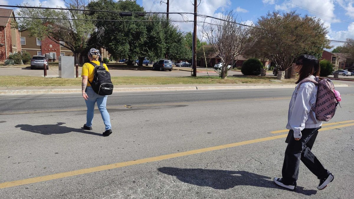 Animal science junior Jackee Corrigan (Left) and piano performance junior Arabella Abrera (Right) cross Aquarena Springs Drive to get to their bus stop, Monday, Oct. 28, 2024, near the Riverside Ranch bus stop.