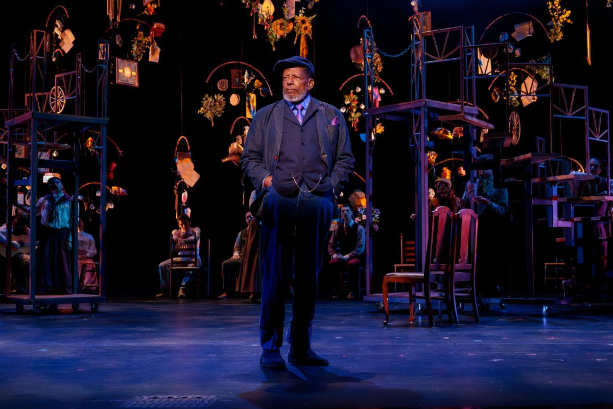 "Our Town" cast members sit and look downstage at program faculty and "Our Town" Stage Manager Eugene Lee, Sunday, Sept. 29, 2024, at the Patti Strickel Harrison Theatre. The set features hanging mobiles of different props representing items mentioned in the play, such as sunflowers, stained glass, letters and heliotropes. Photo courtesy of Lauren Jurgemeyer.