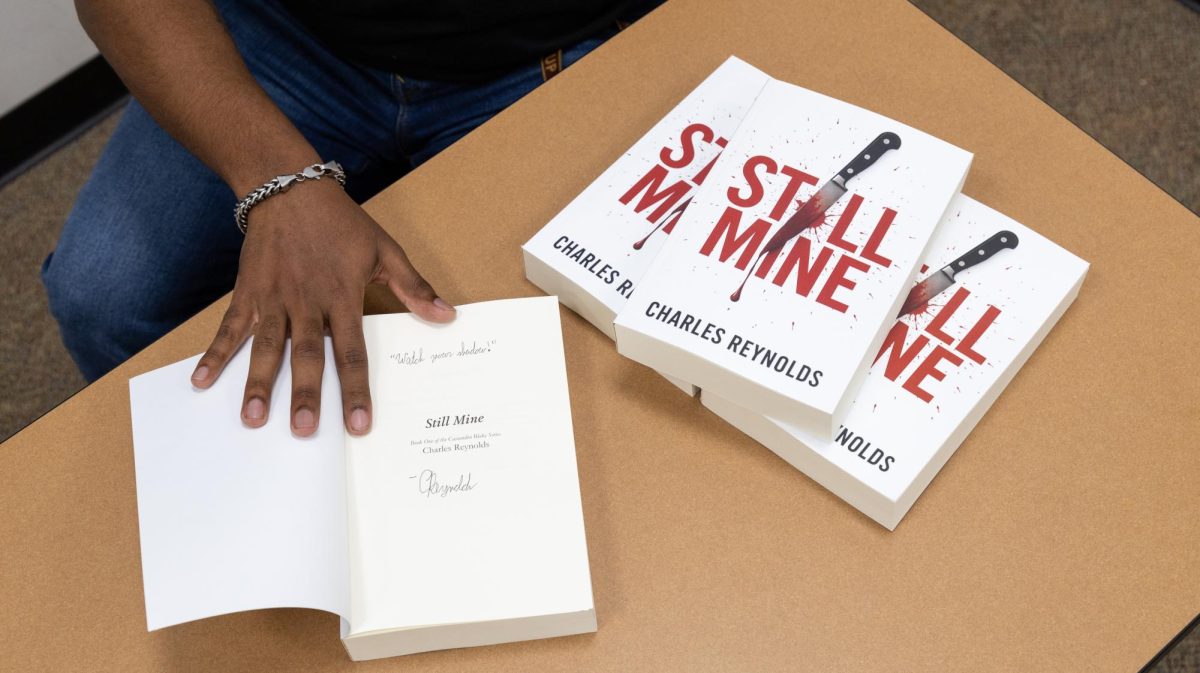 “Still Mine” author Charles Reynolds displays his signed book, Tuesday, Feb. 10, 2026, in Hines Academic Center at 201 State St. The quote above his signature reads “Watch your shadow!"