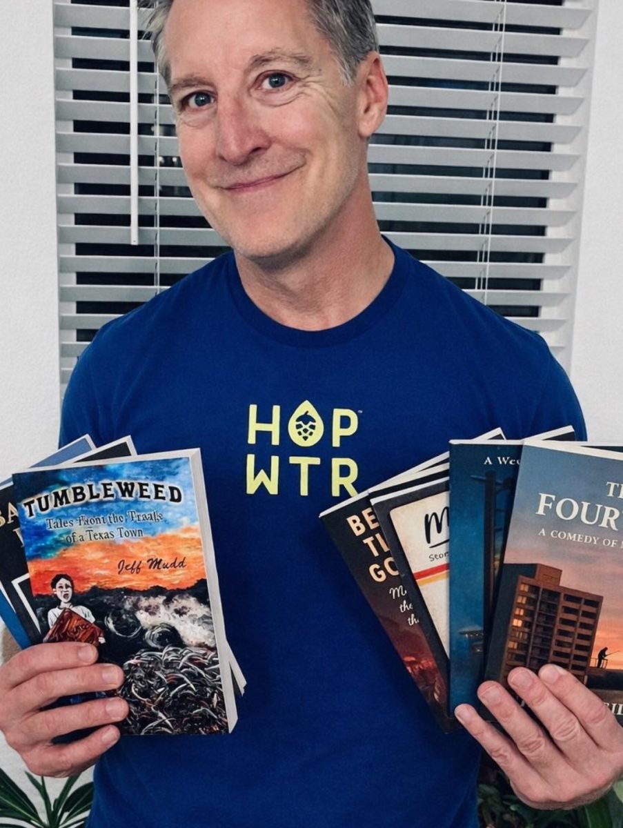 Author and journalism alumnus Jeff Mudd poses with his eight other books, Tuesday, Jan. 13, 2026, in Austin. Photo courtesy of Annie Kelm.